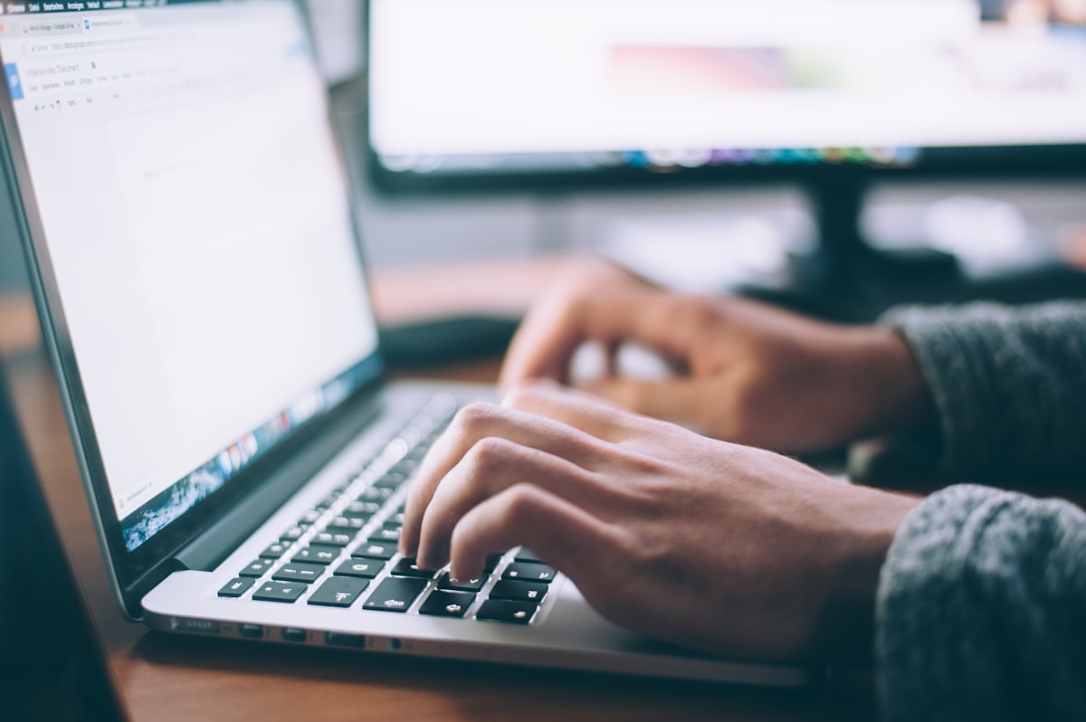 Close-up of hands typing on a laptop at a desk with an external monitor