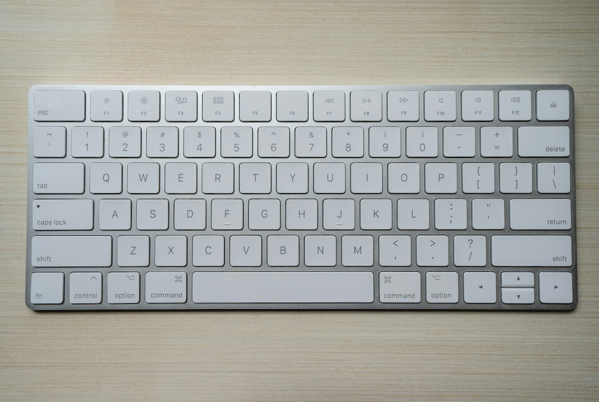 A white wireless keyboard on a wooden desk illustrating a typing setup that affects wrist comfort